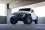 DV8 Offroad 18-23 Jeep Wrangler JL / 20-23 Jeep Gladiator JT FS-7 Mid-Width Winch Front Bumper on white Jeep in parking garage.