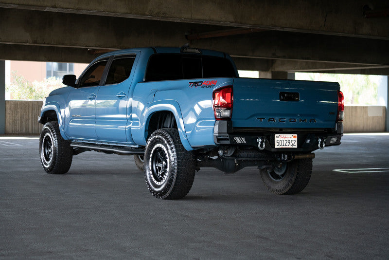 DV8 Offroad 16-23 Toyota Tacoma MTO Series Rear Bumper installed on a blue Tacoma with offroad wheels in a parking garage.