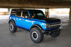 DV8 Offroad 21-22 Ford Bronco OE Plus Series Side Steps installed on a blue Ford Bronco in an urban setting.