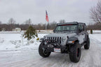 Fishbone Offroad 2018+ Jeep Wrangler JL Windshield Light Bracket on modified gray Jeep Gladiator in snowy landscape.