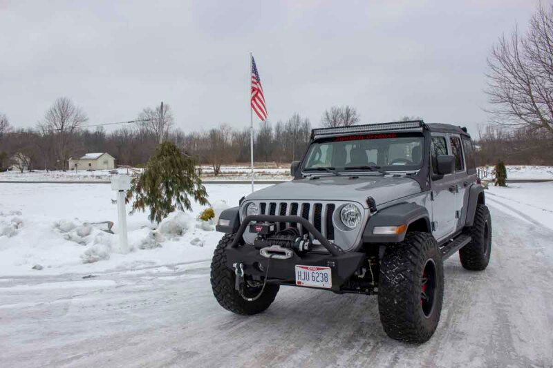Fishbone Offroad 2018+ Jeep Wrangler JL Windshield Light Bracket on modified gray Jeep Gladiator in snowy landscape.