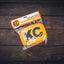 KC HiLiTES Retro 5in x 7in Rectangular Yellow Vinyl Light Cover w/ Black KC Logo (Pair) on wooden background.