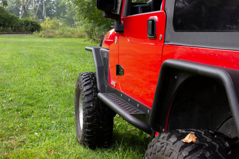 Fishbone Offroad 97-06 Jeep Wrangler TJ Steel Rock Slider - Black Textured Powdercoat on a red Jeep in grass