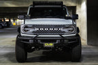 DV8 Offroad 21-22 Ford Bronco Factory Front Bumper Licence Relocation Bracket - Front in parking garage with offroad wheels.