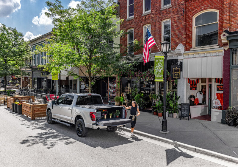 BAK 24-25 Chevrolet Silverado EV 6ft Bed BAKFlip MX4 parked on street with offroad parts and accessories nearby