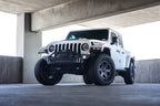 DV8 Offroad 18-23 Jeep Wrangler JL / 20-23 Jeep Gladiator JT FS-7 Mid-Width Winch Front Bumper on white Jeep in parking garage.