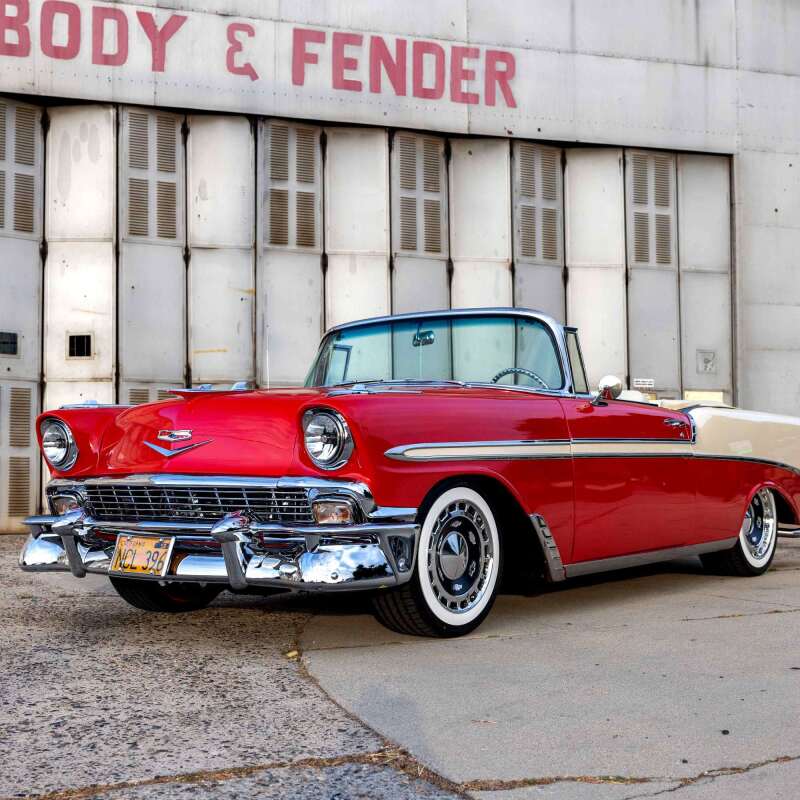 Classic red convertible car parked near a vintage body shop.