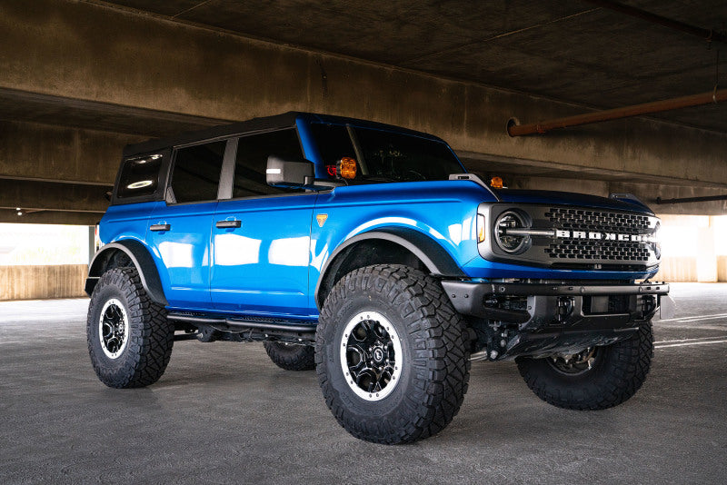 DV8 Offroad 21-22 Ford Bronco OE Plus Series Side Steps on a blue Ford Bronco with offroad wheels in a parking structure.