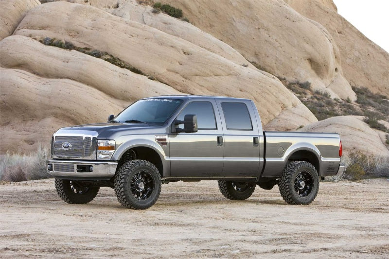 Fabtech 08-10 Ford F250 2WD 6in Basic System - Component Box 1 with offroad wheels on rugged terrain. Main image