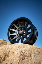 ICON Compression 17x8.5 6x5.5 25mm Offset 5.75in BS 95.1mm Bore Double Black Wheel on rock background.
