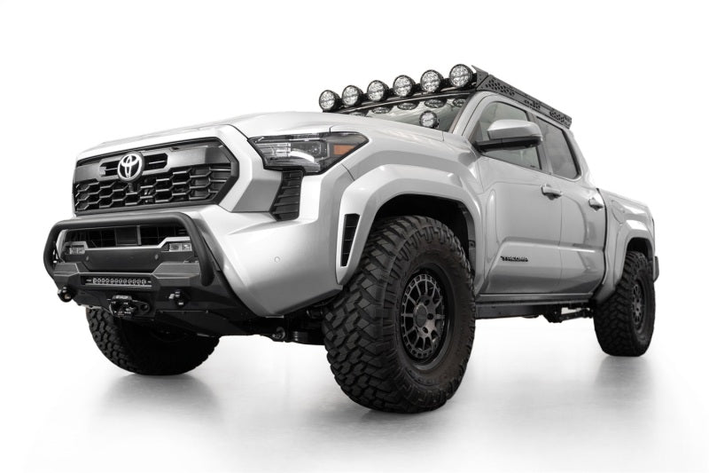 Addictive Desert Designs2024+ Toyota Tacoma Stealth Center Mount Winch Front Bumper w/ Top Hoop with offroad tires and lighting.