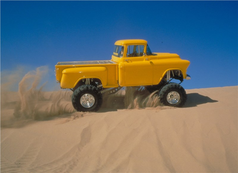 Yellow off road truck navigating sandy dunes with lifted suspension.